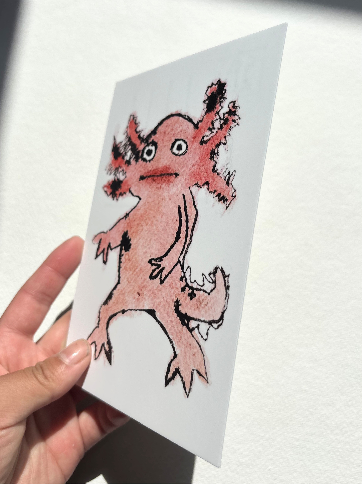 A6 postcard featuring a vivid hand draw watercolour illustration of a cartoon Axolotl.