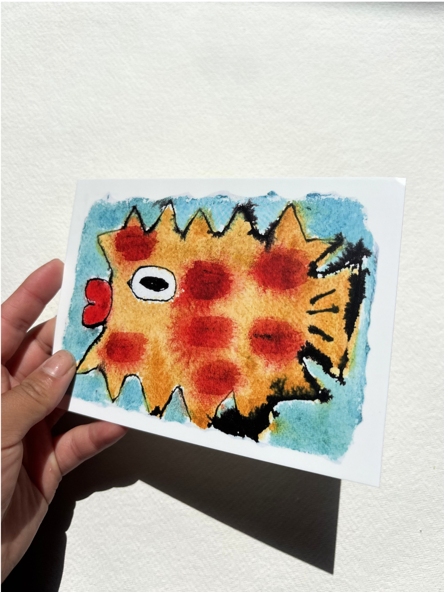 A6 postcard featuring a vivid hand drew watercolour illustration of a puffer fish with blue background.